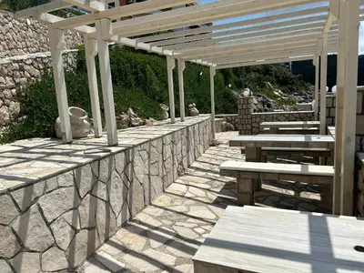 a stone wall with picnic tables and a pergola at Modern apartment with sea view in Dobra Voda, 95 m², Pool in Dobra Voda