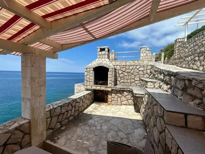 an outdoor patio with a stone fireplace and the ocean at Modern apartment with sea view in Dobra Voda, 95 m², Pool in Dobra Voda