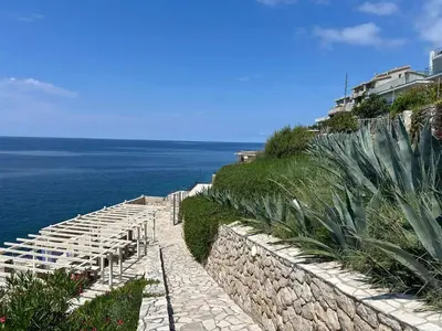 a stone pathway leading to the ocean next to a wall at Modern apartment with sea view in Dobra Voda, 95 m², Pool in Dobra Voda
