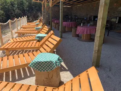 a row of wooden benches with tables and an umbrella at Bigova Glamping in Kotor