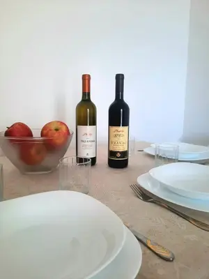 two bottles of wine and a bowl of apples on a table at Acacia apartmani Sutomore in Sutomore