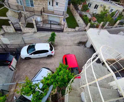 a white car and a red car parked in a parking lot at Apartmani Durovic in Bar