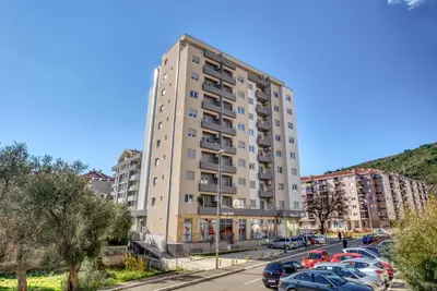 a tall building with cars parked in a parking lot at Baby Blue Apartments in Budva