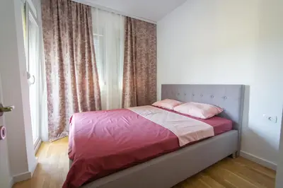 a bedroom with a bed with pink sheets and a window at SUN apartment in Podgorica