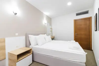 a white bedroom with a white bed and a wooden door at Lux Hotel M in Dobra Voda