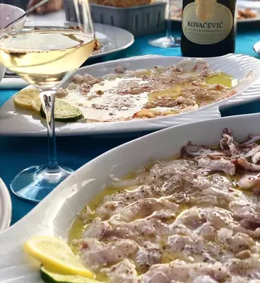 a table with two plates of food and a glass of wine at Apartment Plazza Rafailovici in Rafailovici