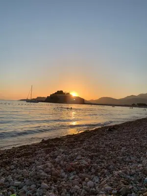 a beach with the sun setting in the background at Pine&Sea Beach Retreat in Sveti Stefan