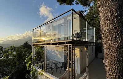 a glass house with a table and chairs on a balcony at House in the pines in Sutomore