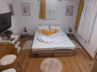a bedroom with a bed with white sheets and yellow pillows at Ljubovic apartman in Podgorica