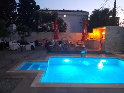 a swimming pool at night with people sitting in chairs around it at Black & White in Sutomore