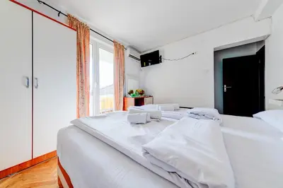 a white bedroom with two beds and a large window at Porta Volta Apartments in Becici