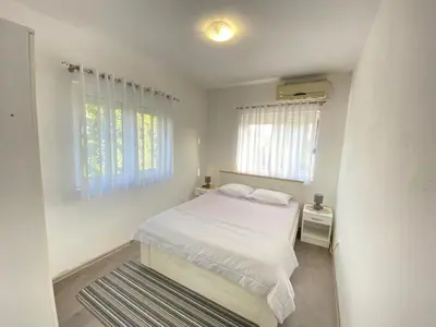 a white bedroom with a bed and two windows at Home Mia Airport in Podgorica