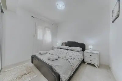 a white bedroom with a bed and a night stand at Apartmani Vittoria in Bar