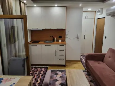 a kitchen with white cabinets and a couch in a living room at Lux Apartmani Bajova in Cetinje