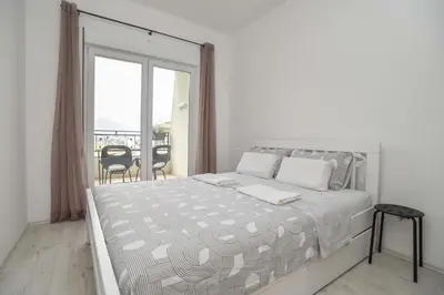 a white bedroom with a large bed and a balcony at Full of light, relaxing, calming apartment in BD in Budva