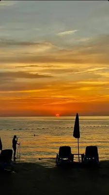 a person standing on a beach with chairs and an umbrella at Horizont Dobre Vode in Dobra Voda