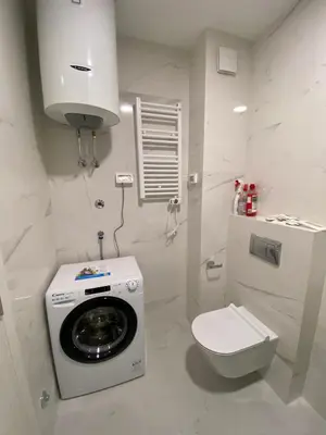 a white bathroom with a washing machine and a toilet at Apartman VT Central point in Podgorica