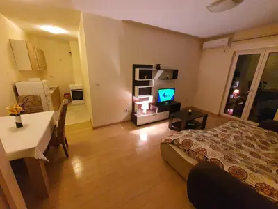 a bedroom with a bed and a table and a kitchen at Clarissa apartment City Kvart in Podgorica