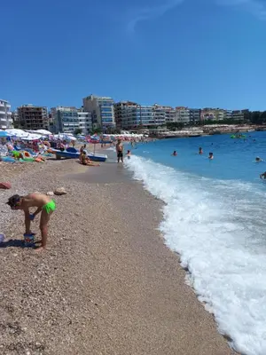 a child standing on a beach with people in the water at Sea View Dobra Voda in Dobra Voda