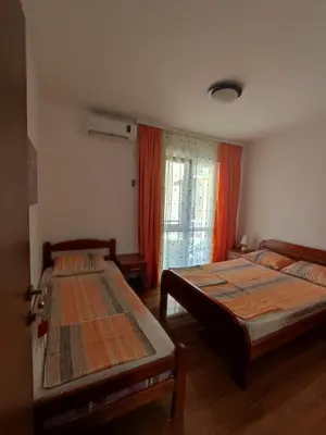 a bedroom with two beds and a window with orange curtains at Apartmani Vuković- Brca in Sutomore