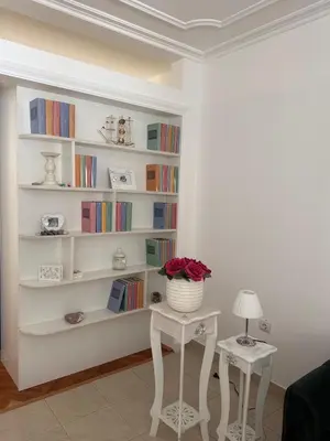 a white book shelf with a vase of flowers on a table at Apartman Na pjenu od mora Becici in Budva