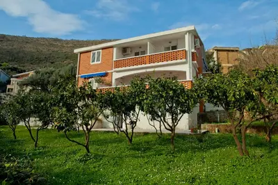 a house on a hill with trees in the foreground at Apartments Mandarina Garden in Petrovac na Moru