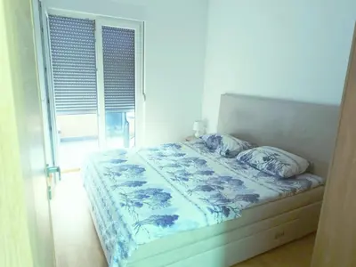 a bedroom with a bed with blue and white sheets and a window at Podgorica apartman in Podgorica