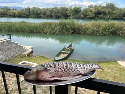 a fish on a plate on a table next to a river at Lotos Luxury House - Skadar Lake in Virpazar