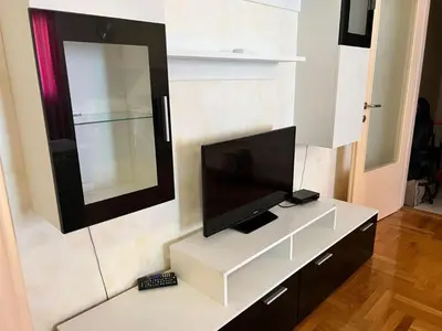 a living room with a television on a white cabinet at Просторная квартира в Петровце с видом на море in Petrovac na Moru