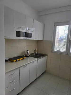a kitchen with white cabinets and a sink and a microwave at Apartman Tološi in Podgorica