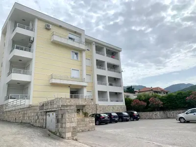 a yellow building with cars parked in a parking lot at Vanilla Apartment Petrovac in Petrovac na Moru