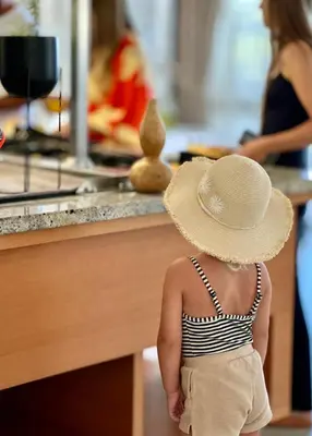 a little girl wearing a hat standing in a kitchen at The New Hotel Mediteran - VILLA Edition in Ulcinj