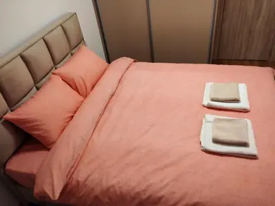 a bed with pink sheets and two towels on it at South Side Apartment in Podgorica