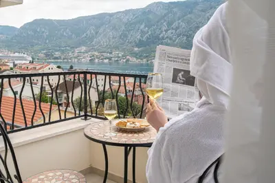 a person sitting on a balcony with a glass of wine at Enyana Luxury Suites in Kotor