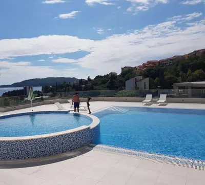 two people are standing next to a swimming pool at Стильная квартира с видом на море и библиотекой in Becici