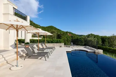 a pool with chairs and umbrellas next to a house at Eterno Villas in Budva