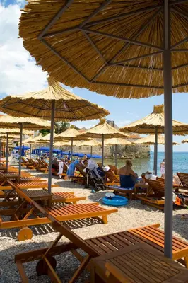 a group of people sitting on a beach with umbrellas at Hotel Astoria in Budva