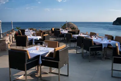 a restaurant with tables and chairs and the ocean at Hotel Astoria in Budva
