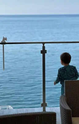 a little boy standing next to the water looking at a cat at Paradise beachfront view 1 in Bar