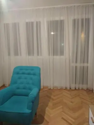 a blue chair in a room with white curtains at Main bus station apartment in Podgorica