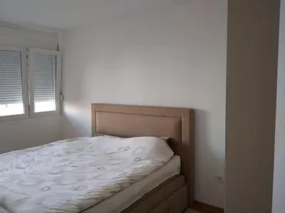 a bed in a white bedroom with a window at Main bus station apartment in Podgorica