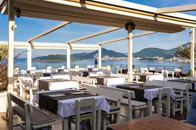 a restaurant with white tables and chairs and the water at Hotel Adrović in Sveti Stefan