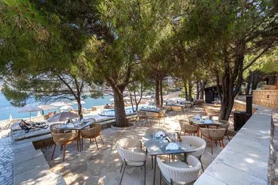 a restaurant with tables and chairs and trees and water at Radisson Resort Ruza Vjetrova in Dobra Voda