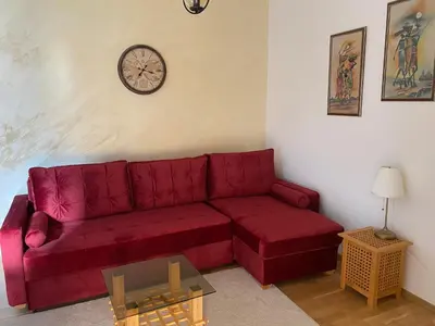 a red couch in a living room with a clock on the wall at Studio Z in Podgorica