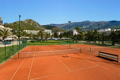 a tennis court in a city with palm trees and mountains at Iberostar Waves Bellevue All Inclusive in Budva