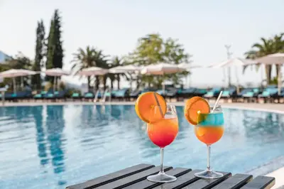 two cocktails sitting on a table next to a swimming pool at Iberostar Waves Bellevue All Inclusive in Budva