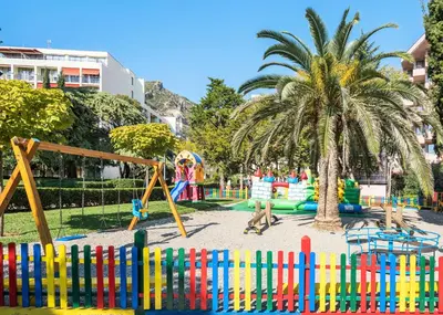 a playground in a park with a palm tree and a fence at Iberostar Waves Bellevue All Inclusive in Budva