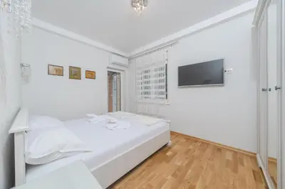 a white bedroom with a bed and a flat screen tv at Markoni Apartments in Budva