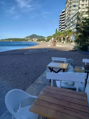 a table and chairs on a beach with a table and benches at Perovic 23 in Rafailovici