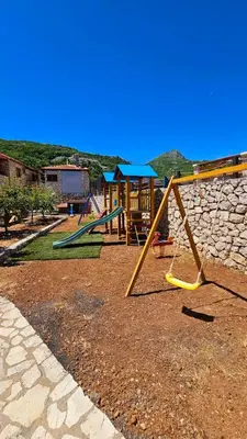 a playground with two swings and a stone wall at Vinogradina Eco Vukčević in Virpazar